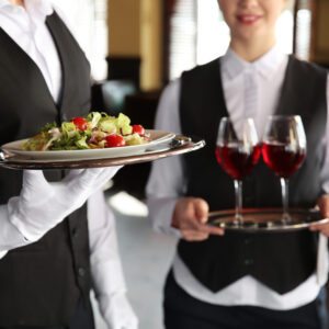 Two waitresses holding trays of food and wine.